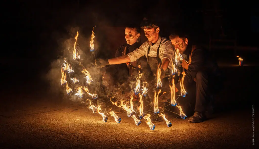 Trio de jongleurs exécutant une chorégraphie pyrotechnique synchronisée avec des éventails de feu lors du spectacle Étincelle Mécanique en province de Liège.